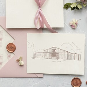 Op de afbeelding: Een roze envelop met een witte binnenenvelop en een witte kaart met een lijntekening van een schuur. De envelop heeft een zegel van was met een bladerenontwerp. De kaart ligt op een wit oppervlak met een gouden stempel en een roze lint.