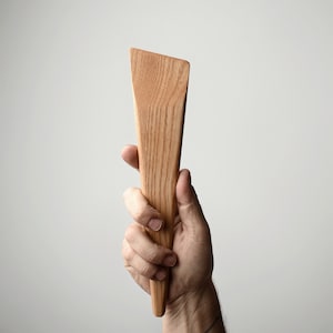 May include: A wooden spatula with a long, narrow, pointed blade. The spatula is made of light brown wood with a natural grain pattern.