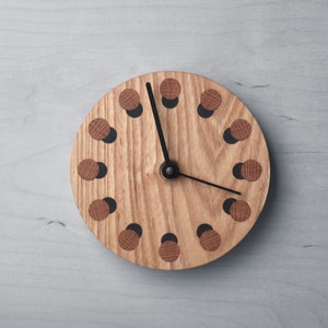 Könnte beinhalten: Eine Holzuhr mit schwarzen Zeigern und einem einzigartigen Design mit einer Reihe von schwarzen und braunen Kreisen um das Zifferblatt.
