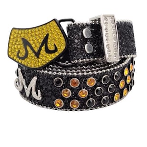 May include: A black belt with a silver buckle and a yellow rhinestone buckle with the letter "M" in black. The belt is covered in black and yellow rhinestones.