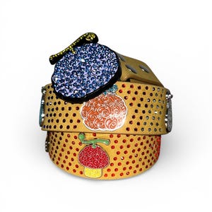 May include: A tan belt featuring a pattern of small red rhinestones and several colourful metal charms shaped like stylised fruits. The charms include a large blue crystal-encrusted piece, an orange swirl design, and a red and yellow mushroom-like shape.