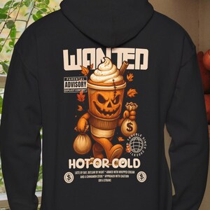 Puede incluir: Sudadera con capucha negra con un diseño temático de calabaza. El diseño presenta una taza de café con una cara de jack-o'-lantern, hojas de otoño y los textos "WANTED" y "HOT OR COLD".