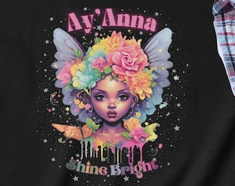 May include: Black t-shirt with a colorful illustration of a girl with flowers in her hair and butterfly wings. The text "Ay'Anna Shine Bright" is printed below the illustration.