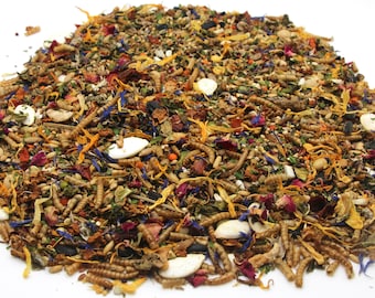 May include: A close-up of a mixture of dried insects, seeds, and flowers. The mixture is a light brown colour with hints of orange, yellow, and blue. It is a popular food for reptiles and amphibians.