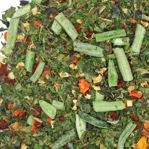 May include: A close-up of a mixture of dried herbs and vegetables, including green leafy herbs, long green strips, and small orange and red pieces.