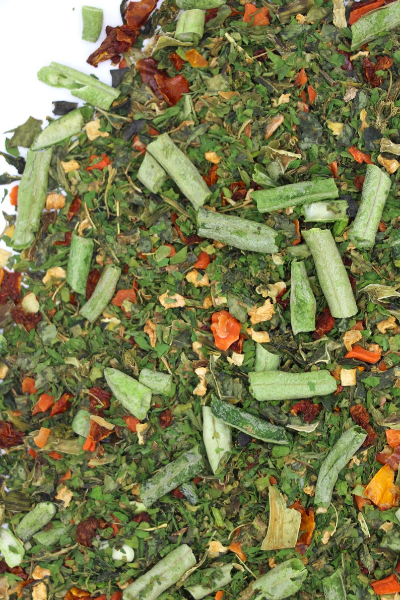 May include: A close-up of a mixture of dried herbs and vegetables, including green leafy herbs, long green strips, and small orange and red pieces.