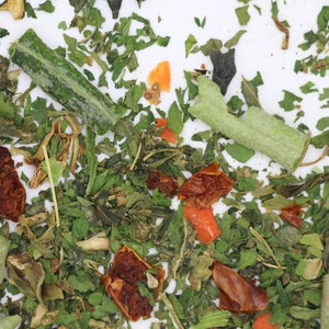 May include: A close-up of a mix of dried herbs and vegetables, including green leafy herbs, dried tomatoes, and orange carrot pieces.