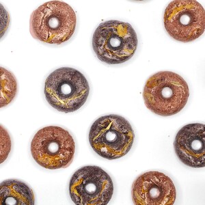 K&ouml;nnte beinhalten: Sortiment von Donuts in verschiedenen Farben und Designs. Die Donuts haben einen glasierten &Uuml;berzug und sind mit goldenen Flocken verziert.