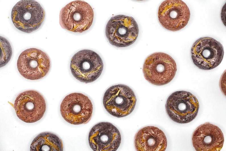 K&ouml;nnte beinhalten: Sortiment von Donuts in verschiedenen Farben und Designs. Die Donuts haben einen glasierten &Uuml;berzug und sind mit goldenen Flocken verziert.
