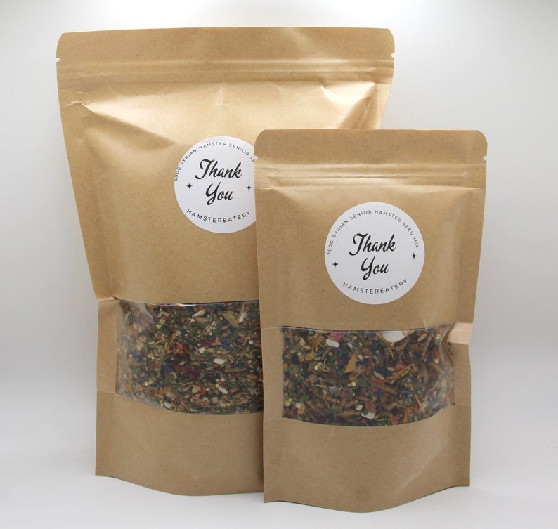 May include: Two brown paper bags with clear windows, each containing a mix of seeds and dried herbs. The bags have white circular labels with the text "Thank You" and "Hamstereatery".