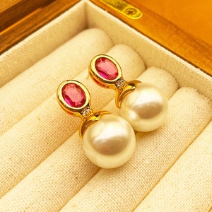 Könnte beinhalten: Ein Paar goldene Ohrringe mit rosafarbenen ovalen Edelsteinen und weißen Perlenakzenten.