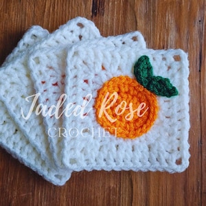 May include: Four square, off-white crochet coasters are stacked. Each coaster has an orange fruit design with green leaves. The text "Jaded Rose Crochet" is visible on the coasters.