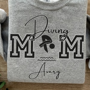 May include: Gray sweatshirt with the text "Diving Mom" in black with a stylized diver graphic and the name "Avery" underneath.