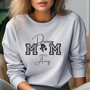 Ash colored sweatshirt featuring the phrase "Diving Mom " and illustrated with a diver. Includes a place to add your diver's name