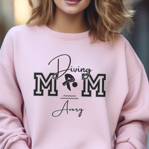 Light Pink colored sweatshirt featuring the phrase "Diving Mom " and illustrated with a diver. Includes a place to add your diver's name