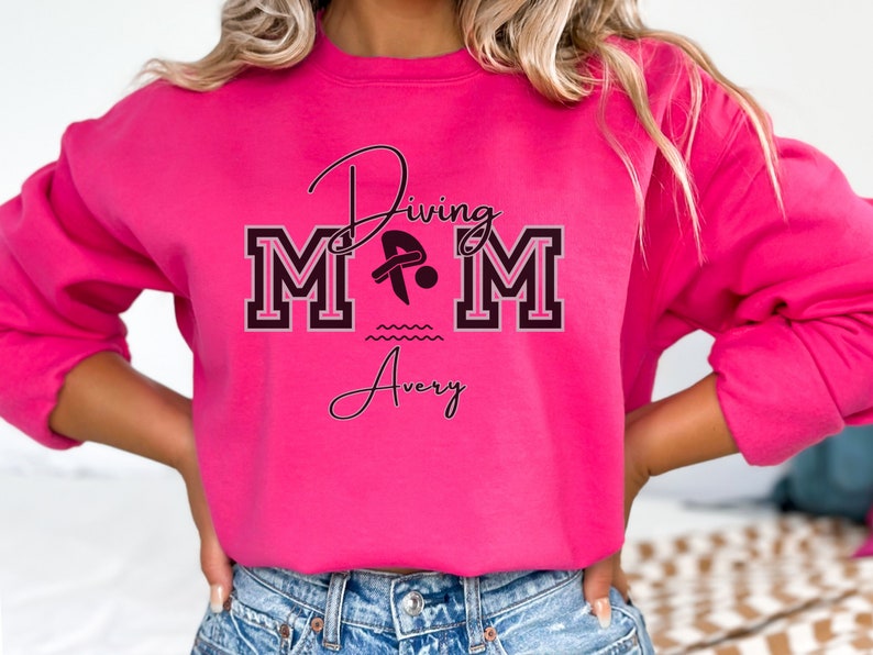 Heliconia (hot pink) colored sweatshirt featuring the phrase "Diving Mom " and illustrated with a diver. Includes a place to add your diver's name