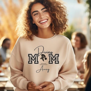 Sand colored sweatshirt featuring the phrase "Diving Mom " and illustrated with a diver. Includes a place to add your diver's name
