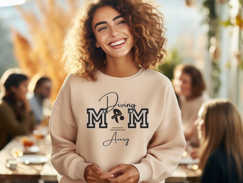 Sand colored sweatshirt featuring the phrase "Diving Mom " and illustrated with a diver. Includes a place to add your diver's name