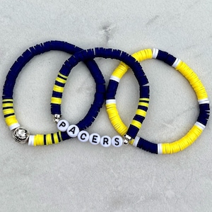 Könnte beinhalten: Drei Perlenarmbänder in Blau, Gelb und Weiß mit einem Basketball-Anhänger und dem Wort "PACERS" in weißen Buchstaben.
