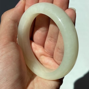 May include: A white jade bangle bracelet. The bangle is smooth and polished, with a slightly off-white color.