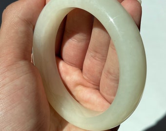 May include: A white jade bangle bracelet. The bangle is smooth and polished, with a slightly off-white color.