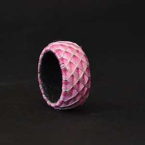 Könnte beinhalten: Ein rosa und weiß gewebter Fingerhut mit schwarzem Innenraum. Der Fingerhut ist in einer traditionellen japanischen Technik namens "Sashiko" gefertigt.