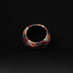 May include: A colorful, circular thimble with a geometric pattern in shades of red, brown, black, and gray.