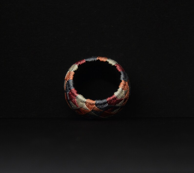 May include: A colorful, circular thimble with a geometric pattern in shades of red, brown, black, and gray.