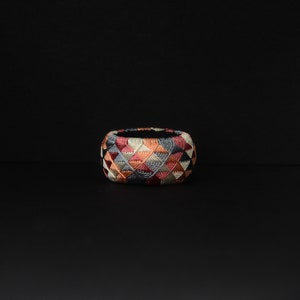 May include: A colorful, geometrically patterned thimble with a black background. The thimble is made of fabric and is embroidered with a variety of colors, including red, pink, blue, and white.