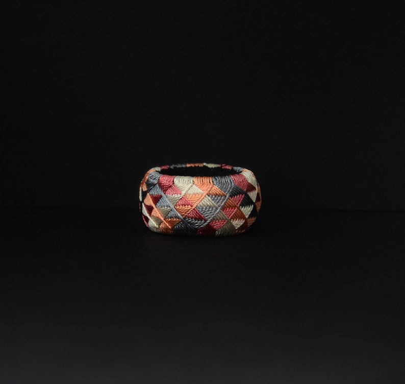 May include: A colorful, geometrically patterned thimble with a black background. The thimble is made of fabric and is embroidered with a variety of colors, including red, pink, blue, and white.