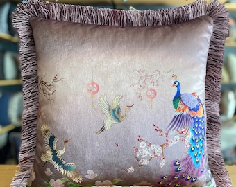 May include: A decorative throw pillow with a purple velvet cover and a fringe border. The pillow features a floral design with peacocks and cranes.