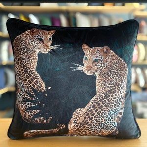 Könnte beinhalten: Schwarzes Samtkissen mit einem Design aus zwei Leoparden in einer Dschungelkulisse. Die Leoparden sind braun und schwarz mit Flecken. Der Hintergrund ist dunkelgrün.