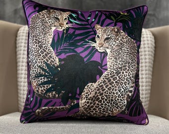 Op de afbeelding: Vierkant decoratief kussen met een paarse achtergrond en een luipaardprint. Het kussen heeft twee luipaarden met bruine en zwarte vlekken, tegen een achtergrond van paars en groen gebladerte.