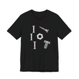 以下が含まれることがあります： 黒いTシャツ。デザインは、ボルト、ネジ、ナットのイラストとともに、3回繰り返される「I」の文字が特徴です。デザインはグレーと白のトーンです。