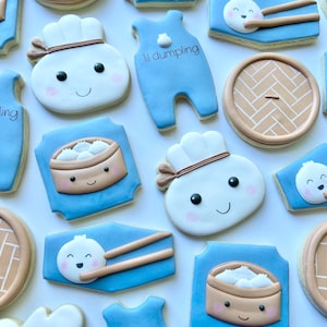 May include: A set of 11 decorated sugar cookies featuring a blue and white baby onesie with the text "lil dumpling", a white dumpling with a brown headband, a brown and white steamed bun, a brown and white bamboo steamer with dumplings, and a brown and white bamboo steamer lid.