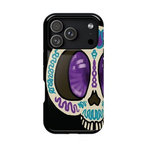 May include: A black phone case featuring a colorful sugar skull design. The skull has large purple eyes, a beige face, and is decorated with blue, purple, and teal accents. The case has a glossy finish and a camera cutout.