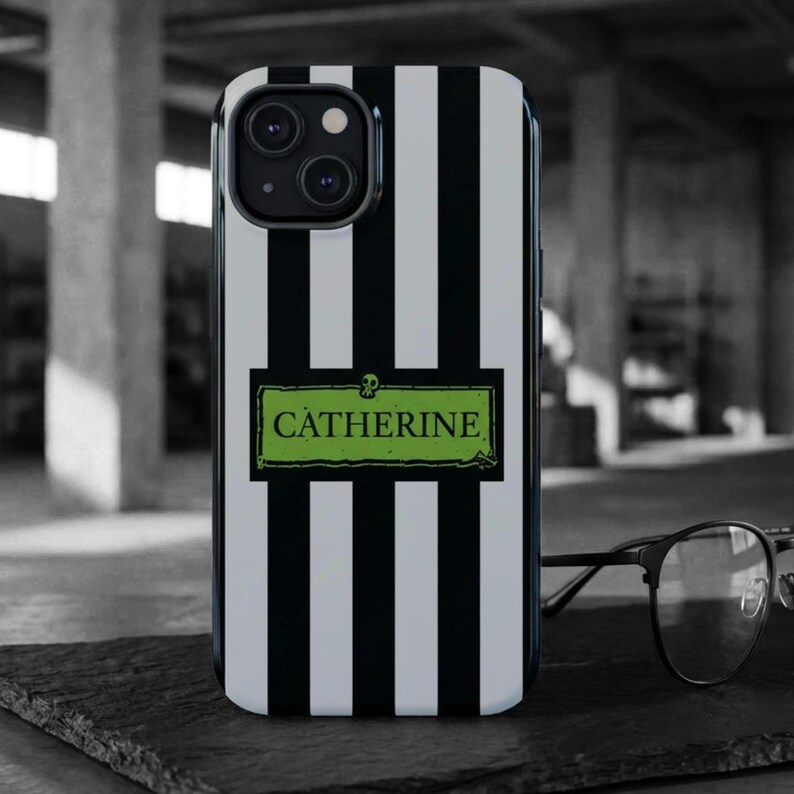A black and white striped phone case with the name "Catherine" in black lettering against a vibrant green background. The case has a skull graphic above the name. The custom phone case is available for iPhone, Samsung Galaxy and Google Pixel and is a perfect personalized gift for her.