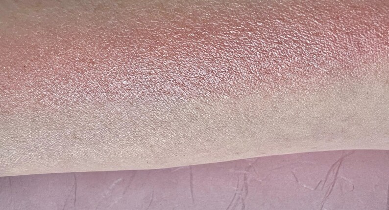 Pu&ograve; includere: Primo piano di un ombretto iridescente scintillante con un gradiente rosa e bianco. L'ombretto ha una texture fine e glitterata.