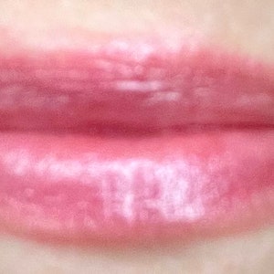 Pu&ograve; includere: Primo piano di labbra che indossano un lucidalabbra trasparente rosa con un finish shimmer.