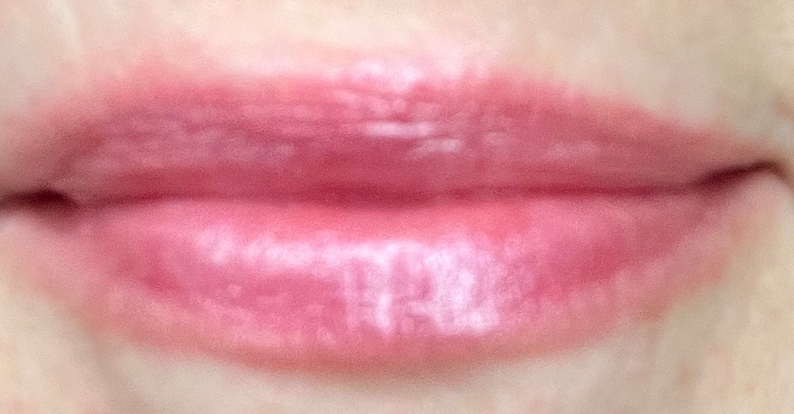 Pu&ograve; includere: Primo piano di labbra che indossano un lucidalabbra trasparente rosa con un finish shimmer.