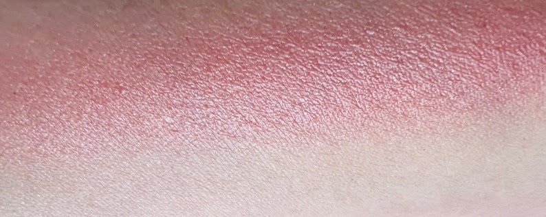 Pu&ograve; includere: Un primo piano di un campioncino di ombretto rosa e bianco sulla pelle. L'ombretto ha una finitura scintillante.