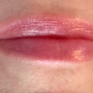 Pu&ograve; includere: Primo piano di labbra di una persona con un lucidalabbra rosa chiaro applicato. Il lucidalabbra ha una finitura scintillante ed &egrave; leggermente applicato in modo irregolare.