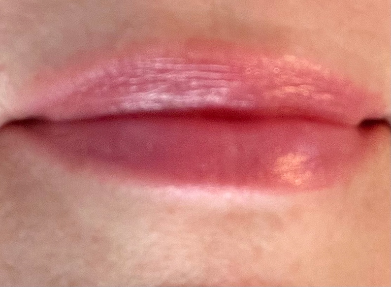 Pu&ograve; includere: Primo piano di labbra di una persona con un lucidalabbra rosa chiaro applicato. Il lucidalabbra ha una finitura scintillante ed &egrave; leggermente applicato in modo irregolare.