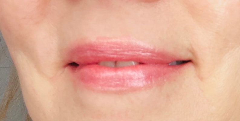 Pu&ograve; includere: Primo piano di labbra che indossano un rossetto rosa chiaro con un leggero luccichio.