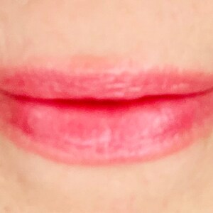 Pu&ograve; includere: Primo piano di labbra con un lucidalabbra rosa chiaro applicato.