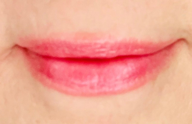 Pu&ograve; includere: Primo piano di labbra con un lucidalabbra rosa chiaro applicato.