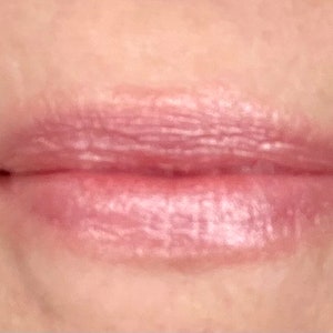 Pu&ograve; includere: Primo piano di labbra che indossano un lucidalabbra rosa chiaro con un finish shimmer.