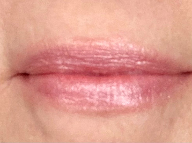 Pu&ograve; includere: Primo piano di labbra che indossano un lucidalabbra rosa chiaro con un finish shimmer.