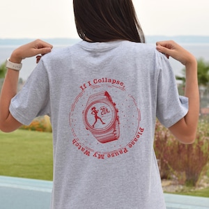 Op de afbeelding: Grijs T-shirt met een rode afbeelding van een horloge met een hardlopende figuur en de tekst "Als ik ineenstort, pauzeer dan mijn horloge"