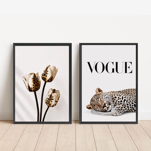 May include: Two framed wall art prints in black frames. The left print features three tulips with white petals and brown leopard print spots. The right print displays a leopard lying down wearing a crystal necklace with the word VOGUE above it.